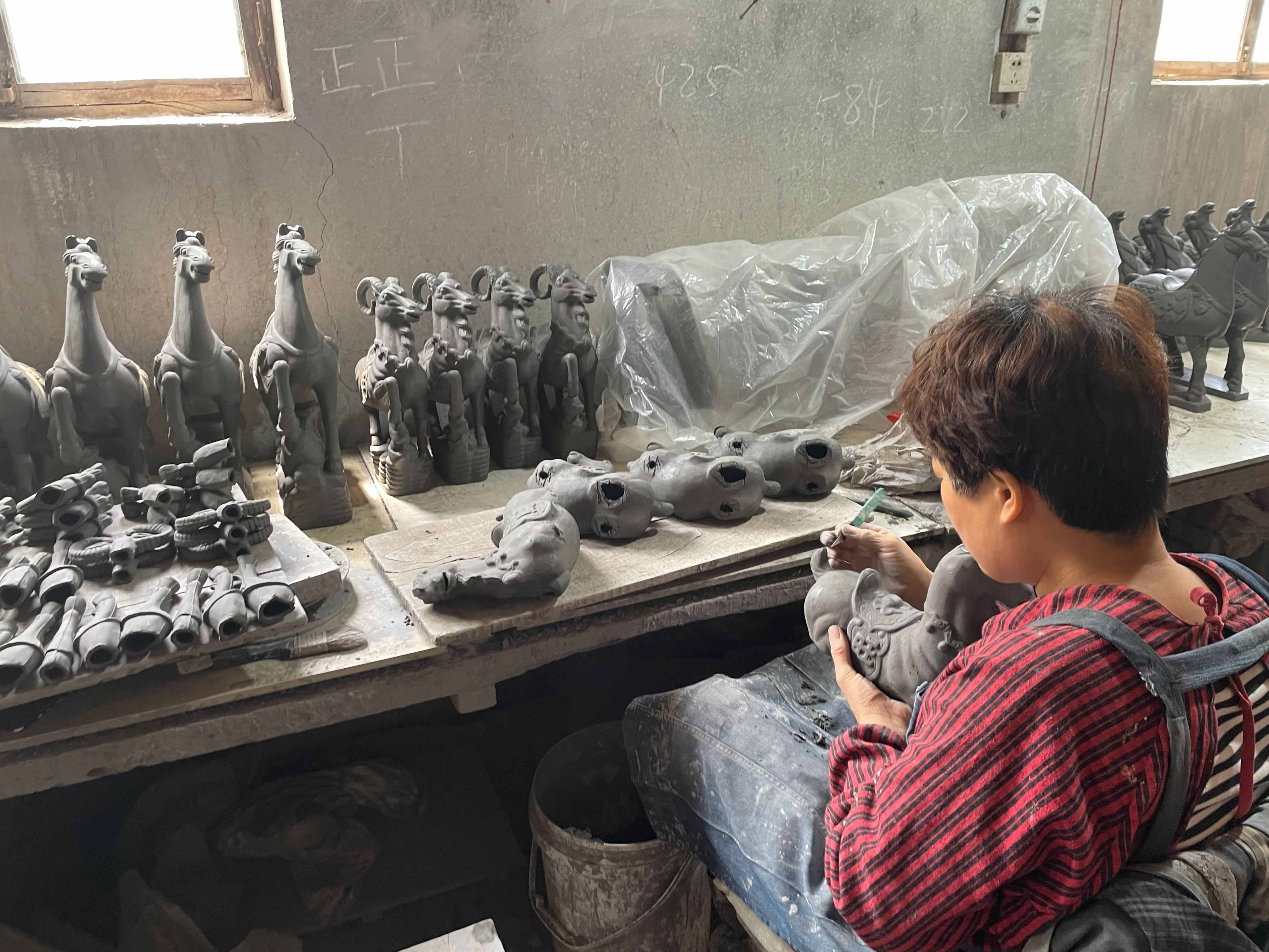 An artisan hand-building a small clay horse at a workbench